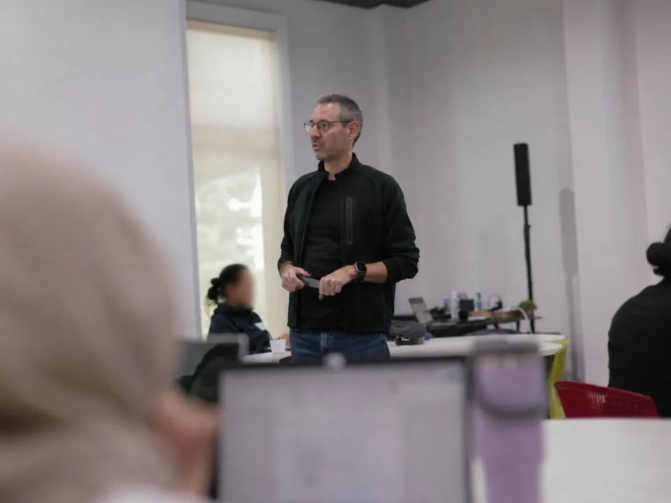 Tom leading a session, standing among participants working at laptops