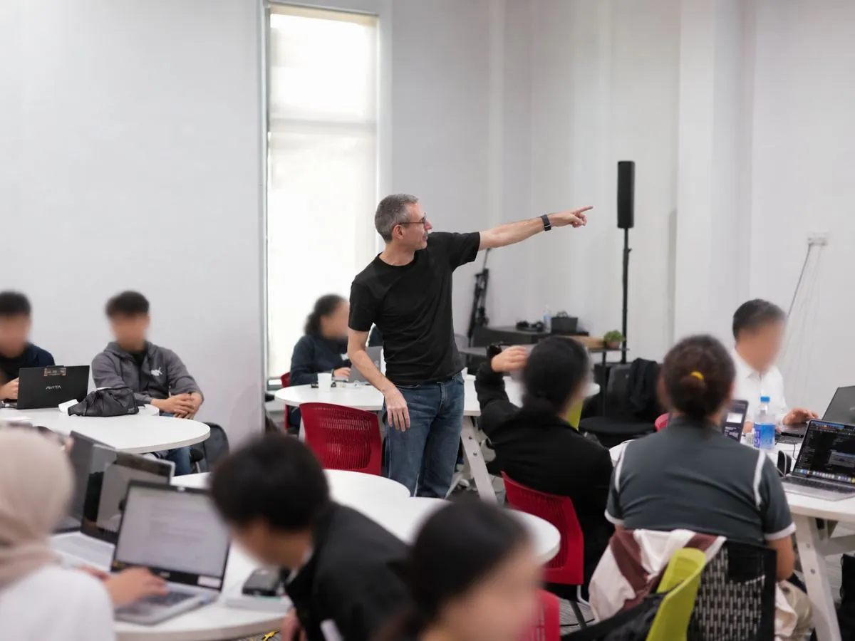 Tom pointing to the board while participants work on laptops in a bright classroom